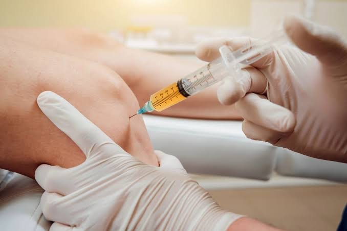 Close-up of a healthcare professional wearing gloves administering an injection into a patient's knee with a syringe, illustrating a medical treatment for joint pain, inflammation, or arthritis.