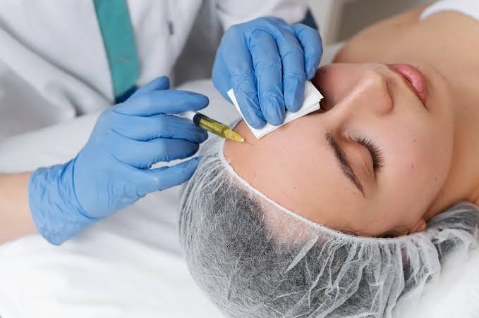 Close-up of a healthcare professional wearing blue gloves administering a cosmetic injection to a patient's forehead while gently cleaning the treatment area.